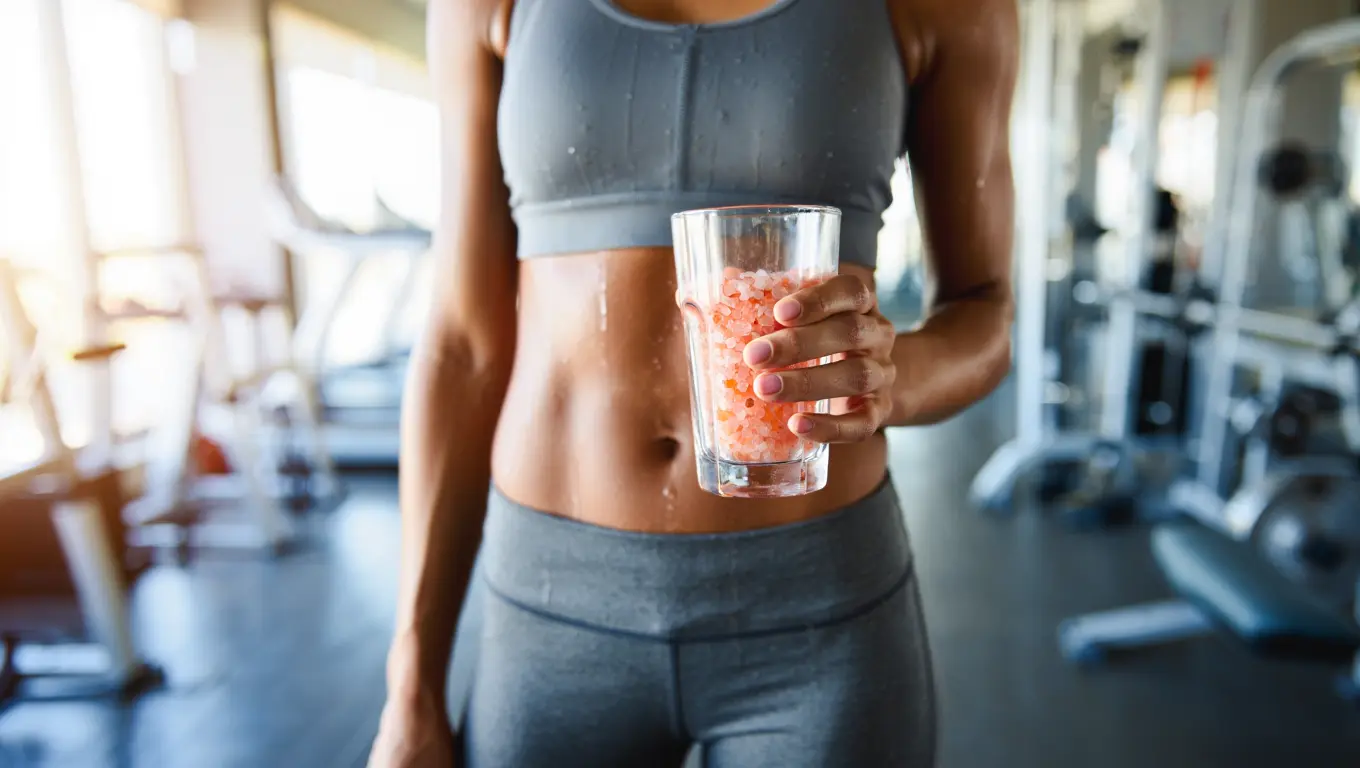 Fit person holding pink salt water glass post-workout in bright gym
