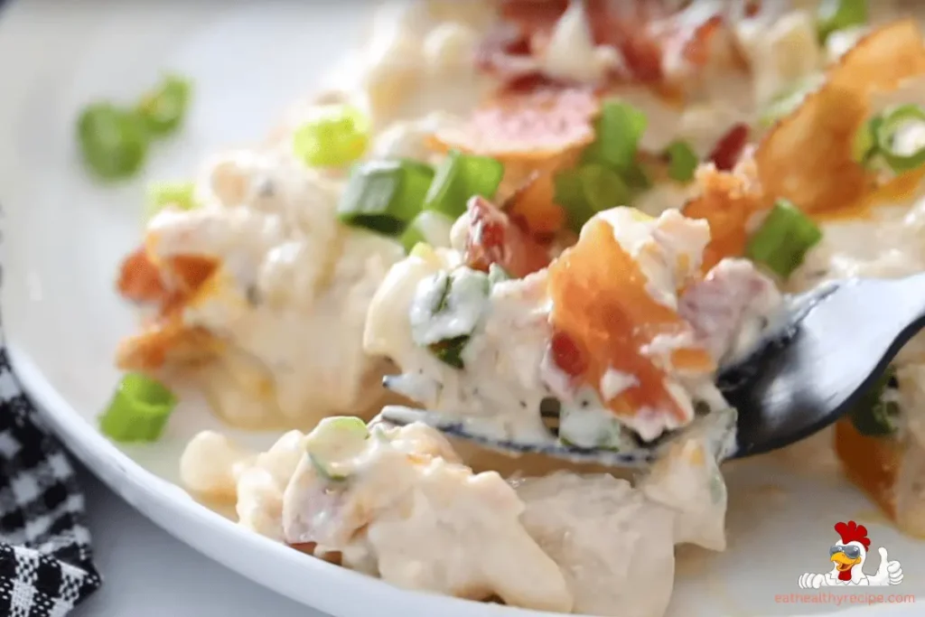 A creamy Crock Pot Crack Chicken Casserole topped with melted cheese, crispy bacon, and green onions in a slow cooker.